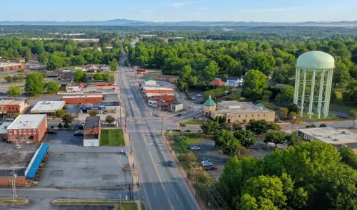 Aerial view of downtown Conover, NC — the main road running between low brick storefronts, the city's green water tower to the right and the Blue Ridge foothills on the horizon