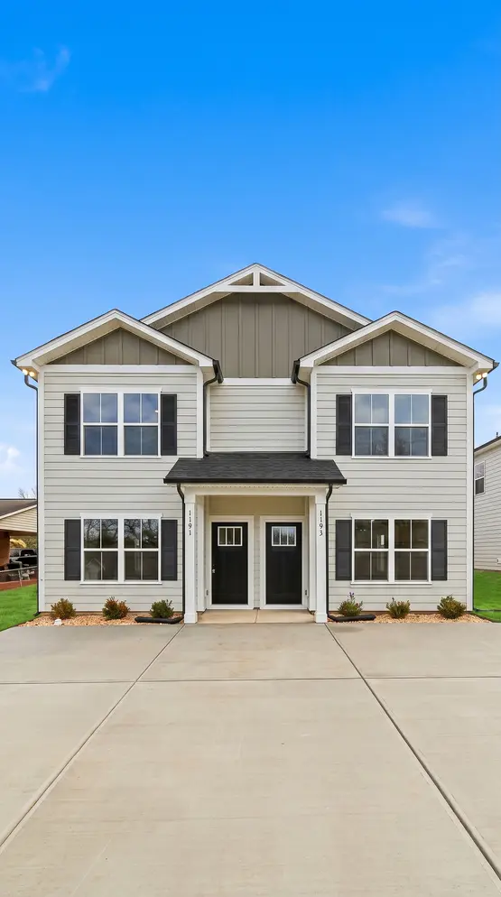 Front elevation of a Legacy Signature Rentals two-unit home for rent in Conover, NC — beige siding with white trim, black doors and a shared concrete driveway