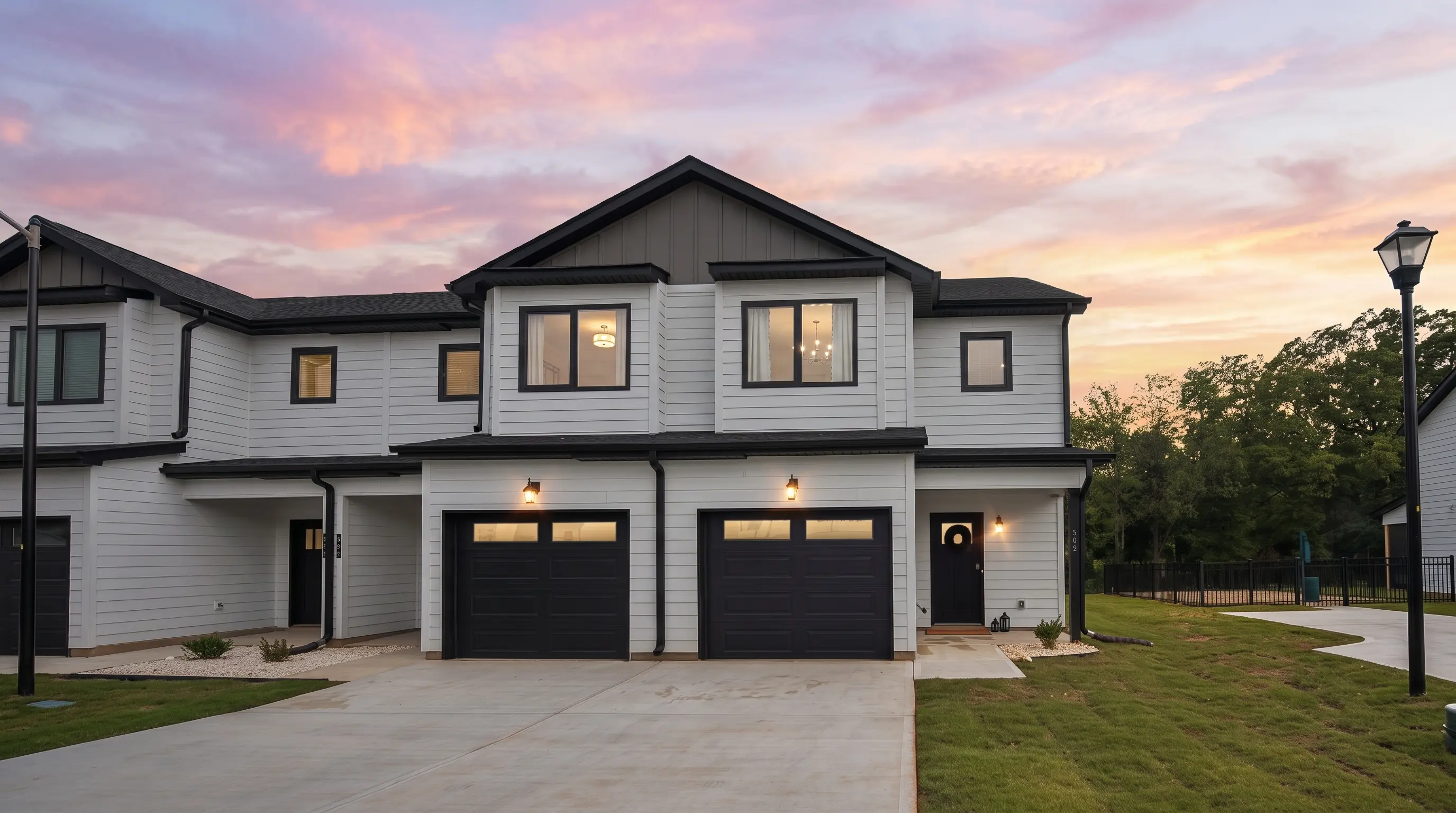 Legacy Signature Rentals townhome at dusk — white siding with black trim and two-car garages