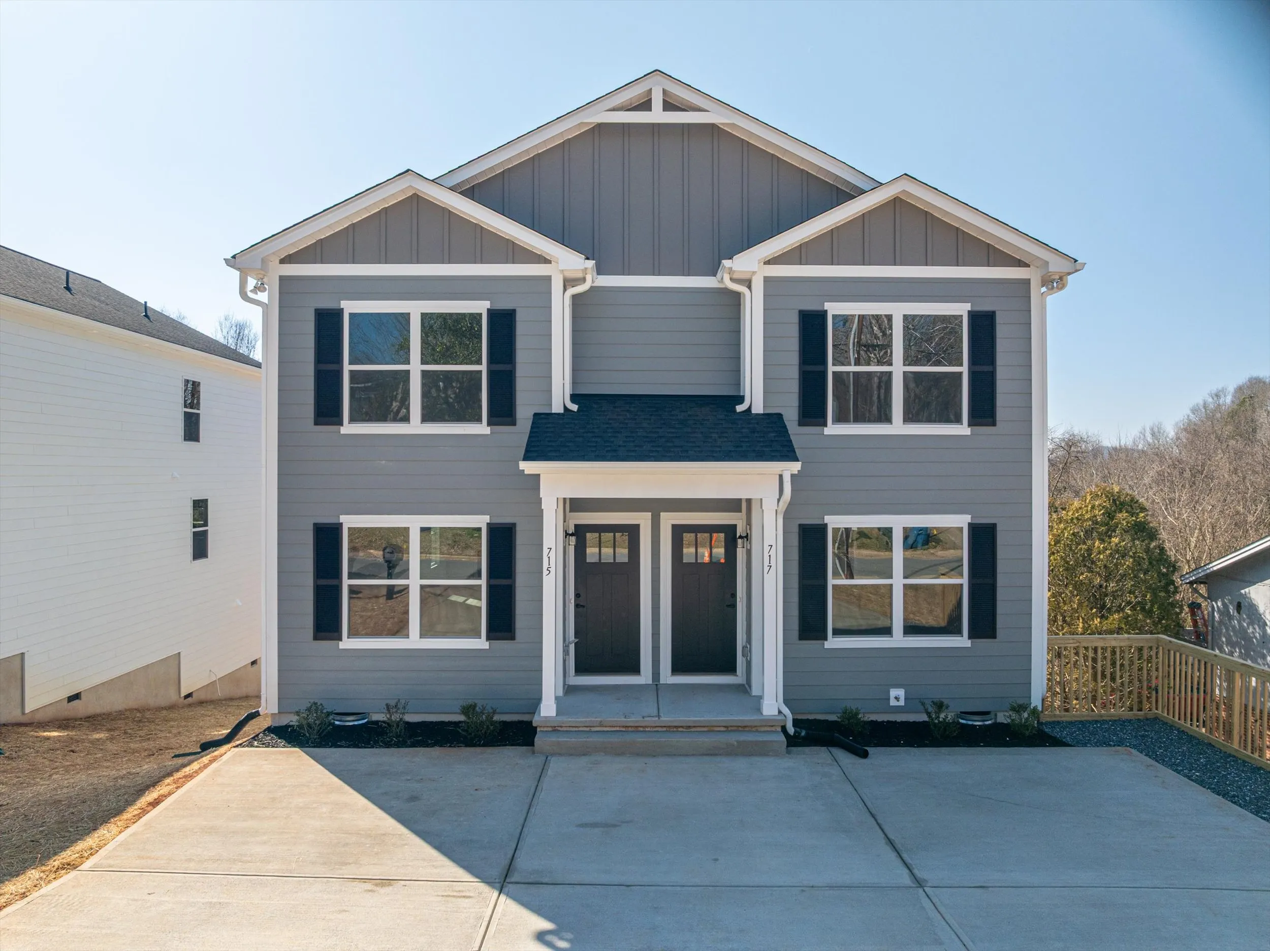 Front elevation of a Legacy Signature Rentals two-unit home for rent — grey siding with white trim, black shutters and two dark front doors side by side under a shared gabled porch, off a wide concrete driveway