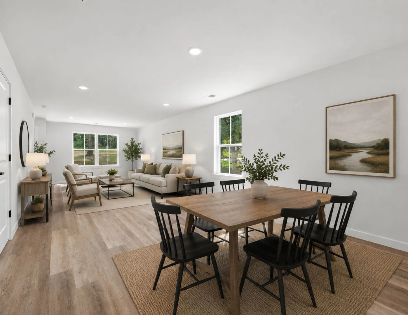 Open-plan living and dining area in a Legacy Signature Rentals home in Hickory, NC — carpet-free plank flooring, a wooden dining table with black spindle chairs, and a sitting area by the windows beyond