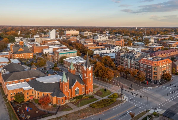 Aerial view of downtown Newton, NC at golden hour — a red-brick church with a tall corner tower on the courthouse square, brick storefronts along the main crossroads and autumn trees through the streets