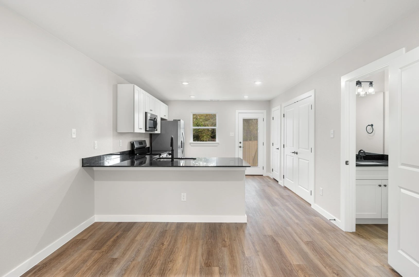 Kitchen and living area in a Legacy Signature Rentals home for rent in Temple, TX — dark granite peninsula counter, white shaker cabinetry, stainless-steel range, microwave and refrigerator, and carpet-free plank flooring